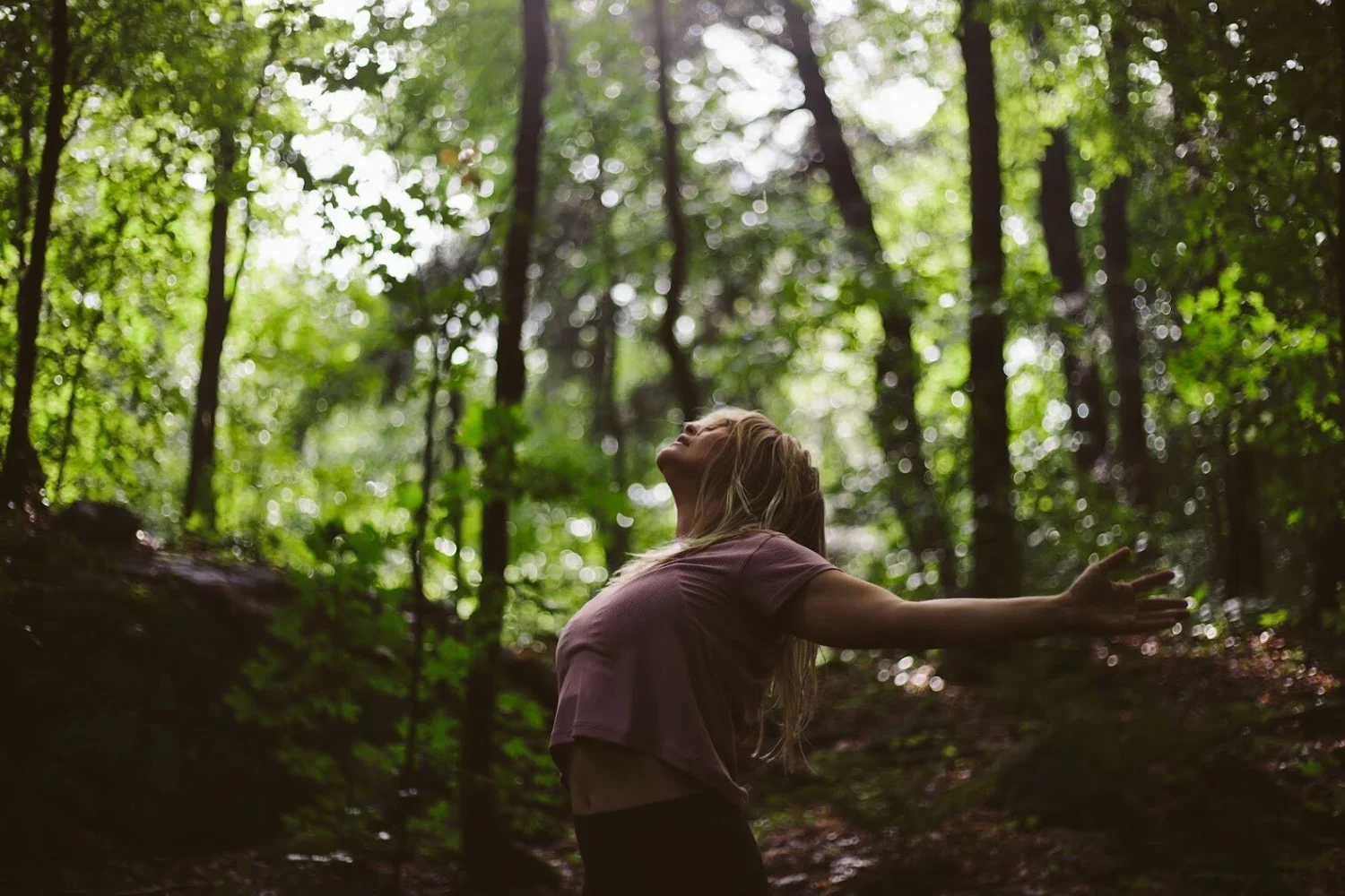 Sam in a forest with arms open, face turned to the sky